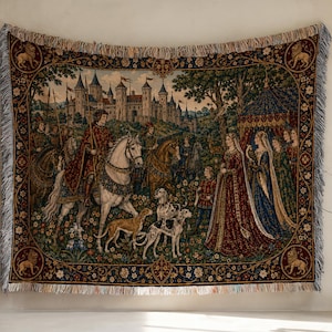May include: Woven tapestry showing a medieval scene with a castle, figures on horseback, and ladies in gowns. The tapestry has a border with floral and lion motifs, and fringed edges. Colours include deep reds, blues, greens, and golds.