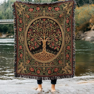 May include: A rectangular woven throw blanket featuring a central circular motif of a tree with intertwined roots and branches. The design includes red roses and green foliage on a black background, finished with a decorative border and fringe.