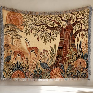 May include: A woven tapestry featuring a savanna landscape with two gazelles, two guinea fowl, a large central tree, and a sun in shades of brown, tan, orange, and blue. The rectangular textile has a fringed border on all four sides with a textured finish.
