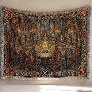 May include: A woven tapestry throw featuring a detailed scene of knights seated around a large round table with a glowing chalice in the centre. The border is decorated with gold lion emblems, blue fleur-de-lis, and floral patterns with fringe.