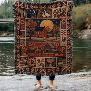 May include: A woven throw blanket featuring a rural autumn scene with a red farmhouse, a barn, horses, pumpkins, sunflowers, and a black cat under a full moon. The border displays geometric star patterns and seasonal motifs with fringed edges.