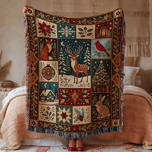 May include: A rectangular woven throw blanket featuring a festive holiday theme with a central deer in a snowy forest. The design includes panels of a fox, a cardinal, a rabbit, a cabin, a Christmas tree, poinsettias, and ornaments with fringe.