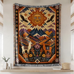 May include: A woven throw blanket featuring a central sun motif, two flying birds, and two llamas standing among stylised flowers and terraced mountains. The design uses a palette of orange, brown, purple, and cream with a fringed border.