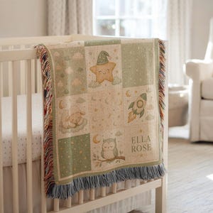 May include: A woven throw blanket featuring a grid pattern with illustrations of a smiling star in a nightcap, a sleeping lamb, a rocket ship, and an owl on a branch. The blanket includes the name ELLA ROSE and has fringed edges on the sides.