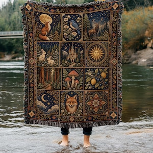 May include: A woven throw blanket featuring a grid of twelve rectangular panels depicting nature scenes including a fox, a deer, a castle, a sun, mushrooms, lemons, and a crescent moon, all set against a dark blue background with fringe.