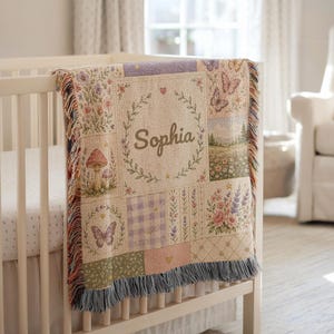 May include: A woven throw blanket featuring a patchwork design with the name Sophia centered in a laurel wreath. The pattern includes illustrations of butterflies, mushrooms, wildflowers, lavender, and a landscape, finished with a fringed edge.