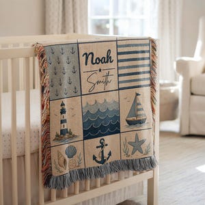 May include: A woven throw blanket featuring a nautical theme with nine panels displaying anchors, stripes, a lighthouse, waves, a sailboat, seashells, and a starfish. The center panel includes the text Noah Smith with a small star graphic.