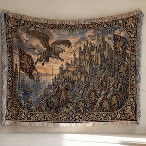Könnte beinhalten: Eine gewebte Wandteppichdecke mit einer detaillierten Szene einer mittelalterlichen Burg auf einer Klippe, einem fliegenden Greifen und gepanzerten Rittern zu Pferd. Der Rand ist mit Löwenmotiven und Blumenmustern verziert und hat Fransen.