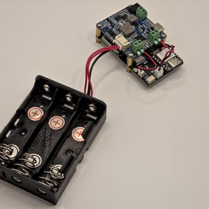 May include: A black plastic battery holder for three 18650 batteries with metal springs and positive terminal markings, connected by red and black wires to a rectangular blue electronic circuit board featuring various components and green connectors.