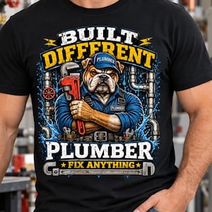 May include: A black t-shirt featuring a graphic of a bulldog dressed as a plumber, wearing a blue cap and shirt, holding a red pipe wrench. The text reads BUILT DIFFERENT, PLUMBER, and FIX ANYTHING, surrounded by metal pipes and water splashes.