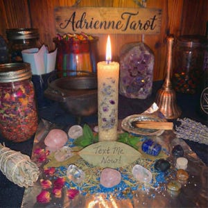 Könnte beinhalten: Eine brennende Kerze mit lila und blauen Akzenten steht auf einem Tisch mit Kristallen, Kräutern und Gläsern. Der Text "Text Me Now!" steht auf einem Blatt. Ein Holzschild darüber lautet "Adrienne Tarot".
