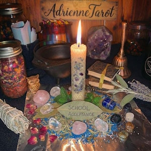 Puede incluir: Una vela encendida con detalles morados se encuentra entre cristales, hierbas y pequeños libros. Un letrero que dice "Adrienne Tarot" está encima de la vela. Las palabras "SCHOOL ACCEPTANCE" están escritas en una hoja. También hay frascos llenos de flores y hierbas secas.