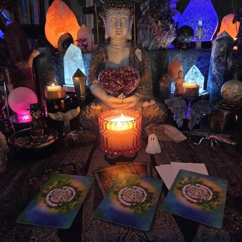 May include: A serene scene featuring a Buddha statue holding a heart-shaped amethyst, surrounded by crystals, candles, and tarot cards. The warm glow of the candles and the crystals create a mystical ambiance. A small ghost figurine is also present.