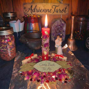 May include: A burning red candle adorned with dried roses and gold leaf, set amidst rose petals, a heart-shaped box, and scrolls tied with red ribbons. A leaf displays the words "Come Back To Me".