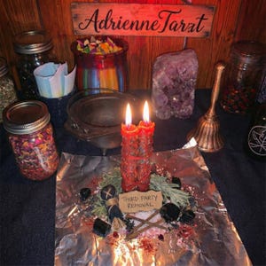 May include: A mystical arrangement featuring a lit red candle, surrounded by herbs, crystals, and ritual items. A sign reads "Third Party Removal." Jars filled with colourful items and a wooden sign with the name "Adrienne Tarat" are in the background.