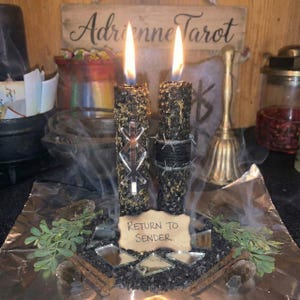 Puede incluir: Dos velas negras encendidas, decoradas con hierbas, un símbolo espejado y alambre de púas. Se apoyan sobre piedras negras con un letrero que dice "Return to Sender". Un letrero de madera dice "Adrienne Tarot".