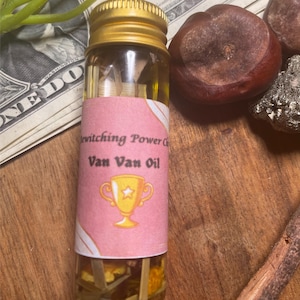 以下が含まれることがあります： 金色のキャップが付いた小さなガラス瓶で、黄色の液体と植物が入っています。「Switching Power」と「Van Van Oil」のピンク色のラベルには、金色のトロフィーのグラフィックが描かれています。瓶は木製の表面にあります。