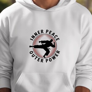 May include: White hoodie featuring a black and red graphic. The graphic is a silhouette of a martial artist kicking, encircled by the words "INNER PEACE" and "OUTER POWER". The hoodie has a drawstring hood and a front pocket.