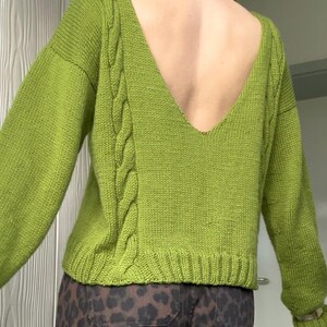 Könnte beinhalten: Ein limettengrüner Strickpullover mit tiefem V-Ausschnitt am Rücken und langen Ärmeln. Der Pullover hat ein Zopfmuster an den Seiten und einen gerippten Saum und Bündchen. Der Rücken ist offen.