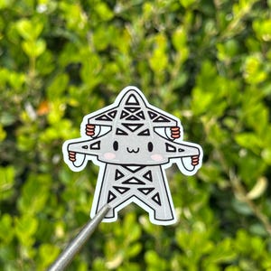 May include: A sticker featuring a cartoon-style electrical pylon with a smiling face and small arms. The pylon is gray with black accents and a white border. The background is a blurred green foliage.