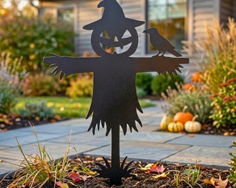 Könnte beinhalten: Schwarzer Metall-Halloween-Vogelscheuchen-Gartenstecker mit einem Kürbisgesicht, einer Krähe auf dem Arm und einem strohähnlichen Rock. Der dekorative Stecker befindet sich in einem Gartenbeet mit Kürbissen und Herbstlaub im Hintergrund.