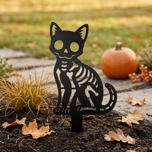 May include: A black metal garden stake shaped like a sitting cat with a skeleton cutout design. The silhouette features hollow eye sockets, a nose cavity, and rib cage details, with a pointed base for insertion into the ground.