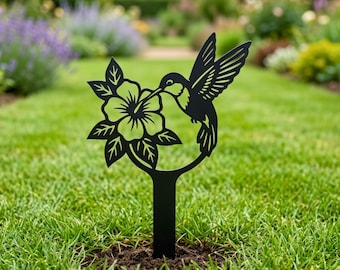 Könnte beinhalten: Schwarzer Metall-Gartenstecker mit einem Kolibri-Motiv. Die Silhouette zeigt einen Kolibri, der sich von einer Blume ernährt. Der Stecker wird in den Boden gesteckt und verleiht einem Garten eine dekorative Note. Der Kolibri ist etwa 25 cm hoch.
