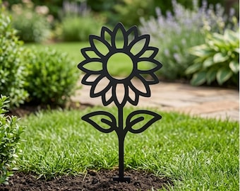 Könnte beinhalten: Ein schwarzer Gartenstecker aus Metall in Form einer stilisierten Sonnenblume mit kreisförmiger Mitte, strahlenförmigen Blütenblättern und zwei symmetrischen Blättern am Stiel. Das flache, ausgeschnittene Design steckt im Gartenboden.