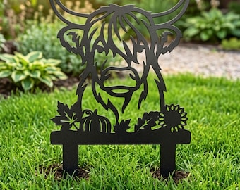 Könnte beinhalten: Ein schwarzer Metall-Gartenstecker mit der ausgeschnittenen Silhouette eines Hochlandrind-Kopfes. Das Design umfasst dekorative Elemente an der Basis, darunter einen Kürbis, ein Ahornblatt, ein Eichenblatt und eine Sonnenblume, gehalten von zwei Stäben.