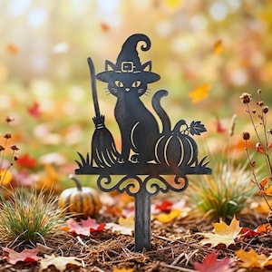 May include: A black metal garden stake featuring a silhouette of a cat wearing a witch hat, standing next to a broomstick and a pumpkin. The design is mounted on a single vertical post with a decorative scrollwork base at the bottom.