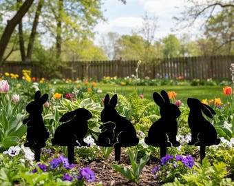 Könnte beinhalten: Schwarze Gartenstecker aus Metall in Hasenform in verschiedenen Posen, darunter eine Mutter und ein Baby. Die Stecker sind in einem Blumenbeet mit bunten Blüten und Grün platziert, mit einem Holzzaun und Bäumen im Hintergrund.