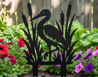 Könnte beinhalten: Schwarzer Metall-Gartenstecker mit einer Silhouette eines Reihers, der zwischen Schilf und hohem Gras steht. Die dekorative Gartenkunst ist für die Platzierung in einem Blumenbeet oder Garten konzipiert. Der Reiher blickt nach links.