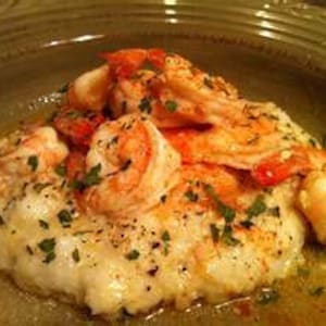 May include: A plate of creamy white grits topped with cooked shrimp and fresh herbs.