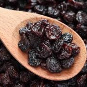 May include: A wooden spoon filled with dark brown raisins, surrounded by a pile of more raisins.