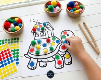 May include: A children's educational activity featuring a turtle outline with colored circles, wooden bowls of colorful pom-poms, and a child's hand placing a blue pom-pom. Includes a pair of wooden tongs and sticker sheets.