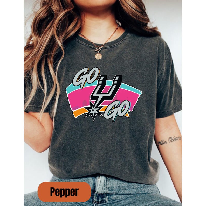 Peut inclure: T-shirt gris fonc&eacute; avec un graphisme color&eacute; &laquo; GO GO &raquo;. Le motif comprend un &eacute;clair stylis&eacute; et une &eacute;toile, avec des touches de rose, de bleu et d'orange. Le t-shirt est de style d&eacute;contract&eacute;.