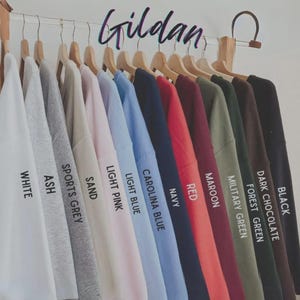 Peut inclure: Pr&eacute;sentation de sweatshirts de la marque Gildan dans diverses couleurs : blanc, gris cendr&eacute;, gris sport, sable, rose clair, bleu clair, bleu Caroline, marine, rouge, bordeaux, vert militaire, vert for&ecirc;t, chocolat noir et noir. Le mot "Gildan" est &eacute;crit en cursive.