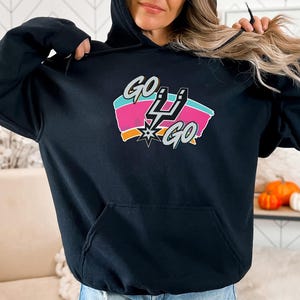 Peut inclure: Sweat-shirt &agrave; capuche noir avec un graphisme color&eacute; qui dit "GO 4 GO". Le graphisme pr&eacute;sente un design stylis&eacute; avec les mots "GO" en blanc, un &eacute;clair et un &eacute;clat d'&eacute;toile.