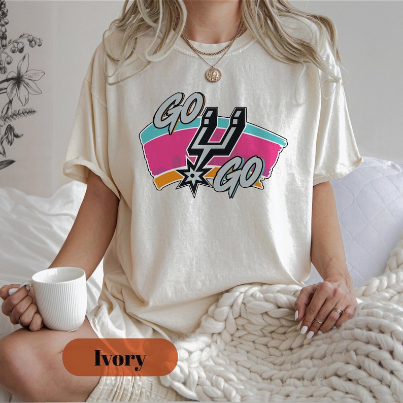 Peut inclure: T-shirt de couleur ivoire avec un graphisme color&eacute;. Le graphisme affiche les mots "Go Go" et un design stylis&eacute; avec des &eacute;l&eacute;ments roses, turquoise, orange et noirs. Le t-shirt est de style d&eacute;contract&eacute;.