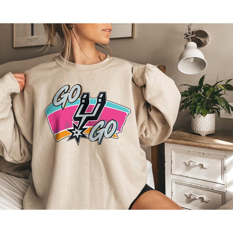 Peut inclure: Sweat-shirt beige avec un motif color&eacute; &laquo;&nbsp;GO GO&nbsp;&raquo; avec un &eacute;peron et un &eacute;clair. Le motif comprend des couleurs rose, turquoise et orange. Le sweat-shirt est de style d&eacute;contract&eacute;.