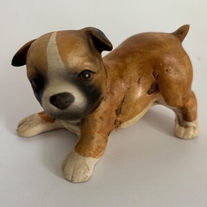 May include: A ceramic Boxer puppy figurine in a playful pose. The puppy has a brown and white coat with black accents around the eyes and ears. The figurine is approximately 4 inches long.
