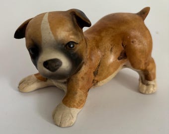 May include: A ceramic Boxer puppy figurine in a playful pose. The puppy has a brown and white coat with black accents around the eyes and ears. The figurine is approximately 4 inches long.