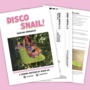 Puede incluir: Un patrón de costura para un adorno colgante "Disco Snail". El patrón incluye instrucciones y diagramas. El adorno es un caracol de fieltro con una concha colorida, antenas rosas y una cara sonriente. El patrón es de Disco Zo.