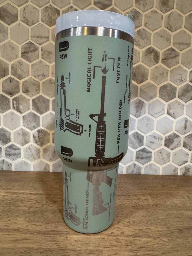 May include: A light green tumbler with a white lid features diagrams of firearms and the phrases "PEW," "MAGICAL LIGHT," and "FAST PEW." The tumbler has a stainless steel rim and a design that includes the text "AIM LOOKY THINGY."