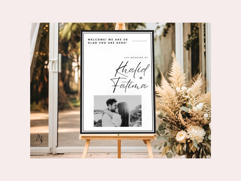 A wedding welcome sign for Khalid and Fatima on a wooden easel placed next to a large arrangement of dried pampas grass and white flowers.