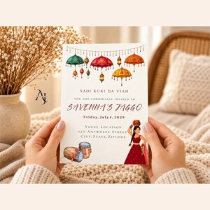 May include: A rectangular invitation card featuring colorful hanging umbrellas and lanterns at the top. The text reads Sadi Kuri Da Viah, You are cordially invited to Savenna's Jaggo, Friday, July 4, 2029, and Venue Location 123 Anywhere Street, City, State, Zipcode.