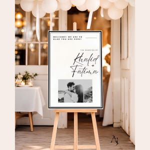 A wedding welcome sign for Khalid and Fatima displayed on a wooden easel indoors with white paper lanterns hanging overhead.
