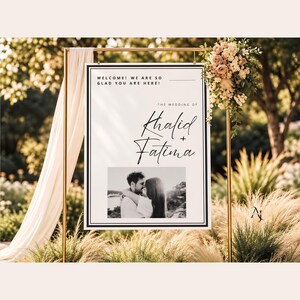 A wedding welcome sign for Khalid and Fatima suspended from a gold metal frame decorated with draping fabric and florals.