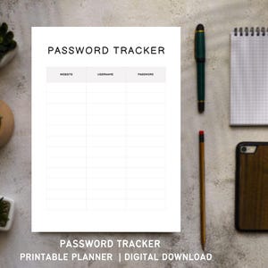 May include: A white Password Tracker printable planner with sections for website, username, and password. A green pen, pencil, notepad, and wooden phone case are arranged around the planner. Small potted plants are in the background.