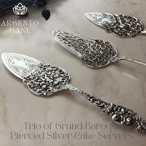 May include: Three ornate silver cake servers with intricate pierced designs. The servers feature detailed floral and scrollwork patterns. The image includes the text "Trio of Grand Baroque Pierced Silver Cake Servers."
